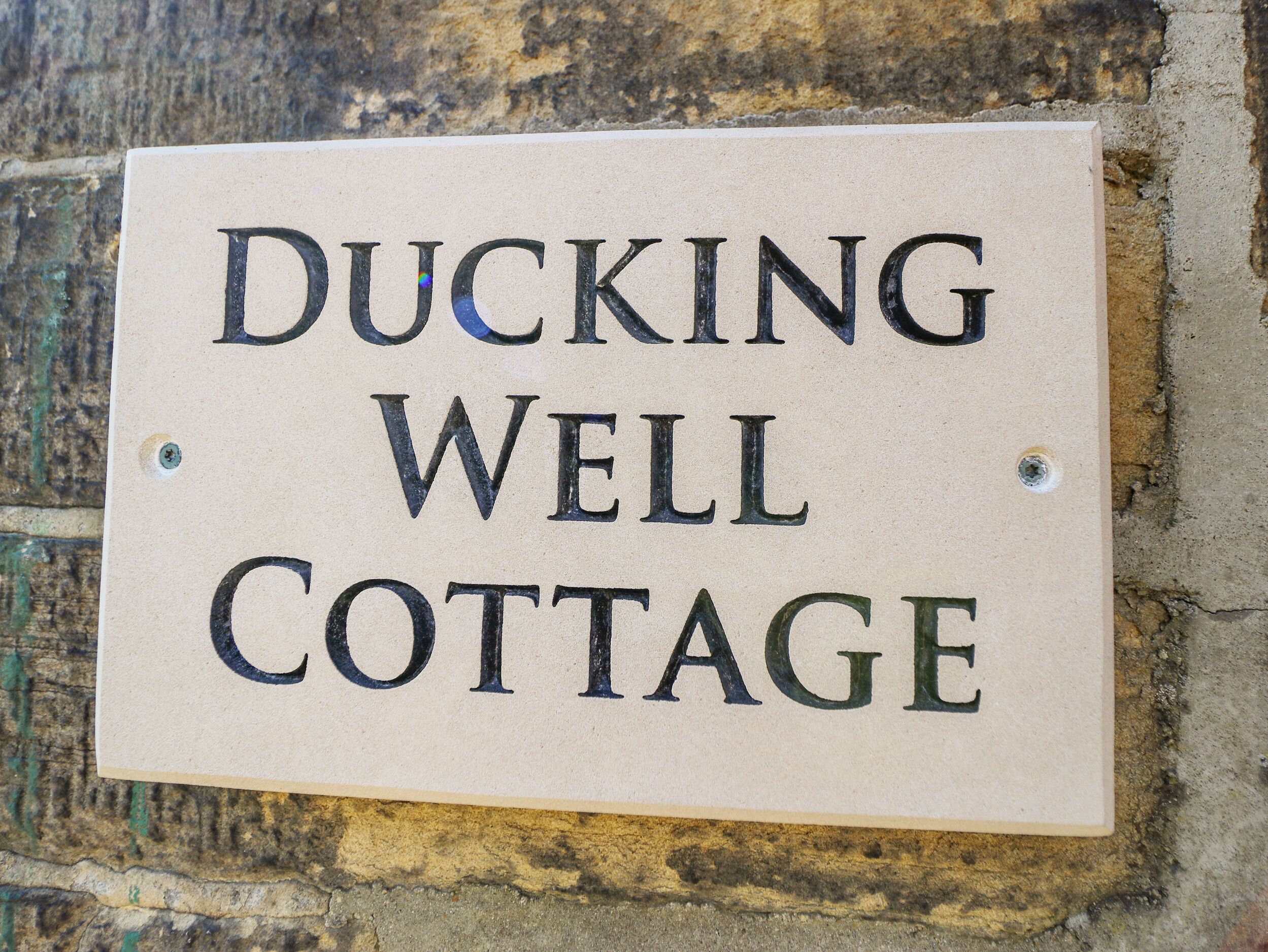 Un letrero con el texto 'DUCKING WELL COTTAGE' colocado en una pared.
