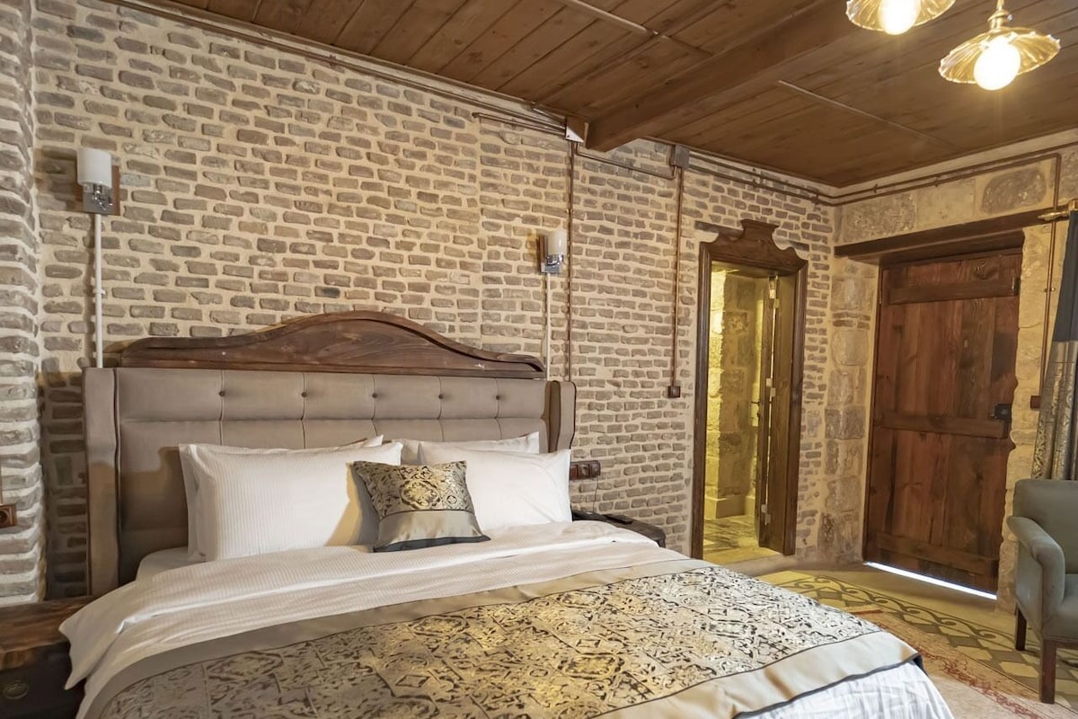 Un dormitorio con pared de ladrillo, techo de madera y cama con ropa de cama estampada.