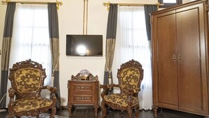 Ein Zimmer mit zwei verzierten Holzstühlen, einem Holzschrank, einem Flachbildfernseher und einem gemusterten Teppich.