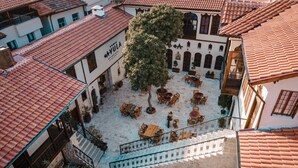 Eine Vogelperspektive zeigt einen Innenhof mit Außenbestuhlung, einer Treppe und einem Gebäude mit einem Ziegeldach.