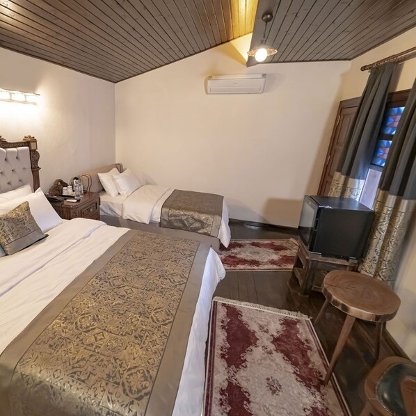 Una habitación de hotel con dos camas, televisor, una mesita y un espejo.