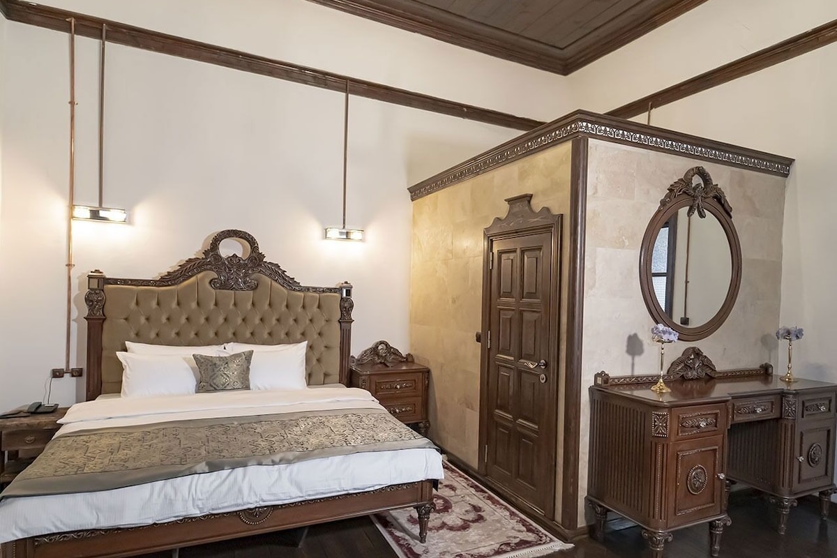 Un dormitorio con una cama grande, cabecera de madera, cómoda con espejo y una araña.