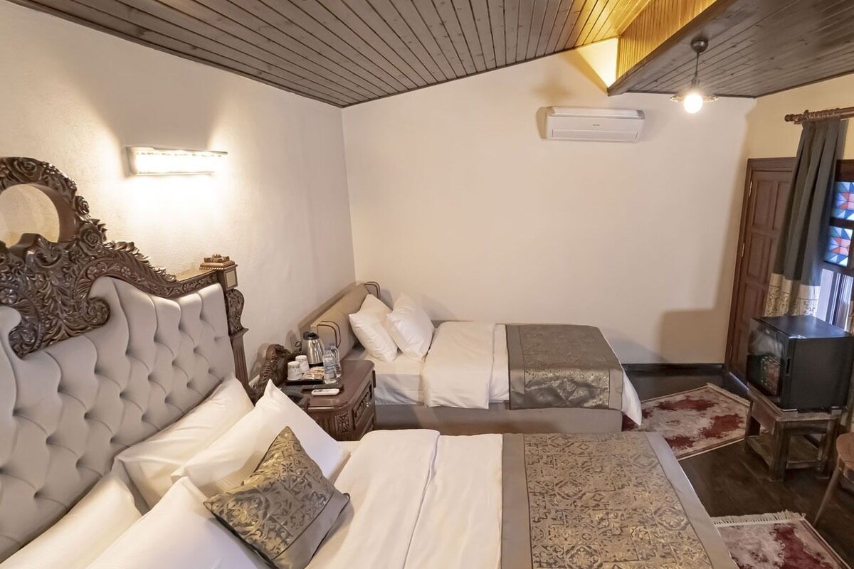 Habitación de hotel con dos camas, techo de madera, televisor y una pequeña mesa con lámpara.