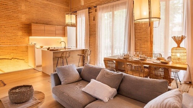 Un vaste espace de vie doté d’un plafond en bois, d’un grand canapé, d’une table à manger et d’une cuisine à l’arrière-plan.