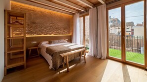 Une chambre à coucher avec un lit, des étagères en bois, un banc et une vue sur une pelouse verdoyante, visible à travers de grandes fenêtres.