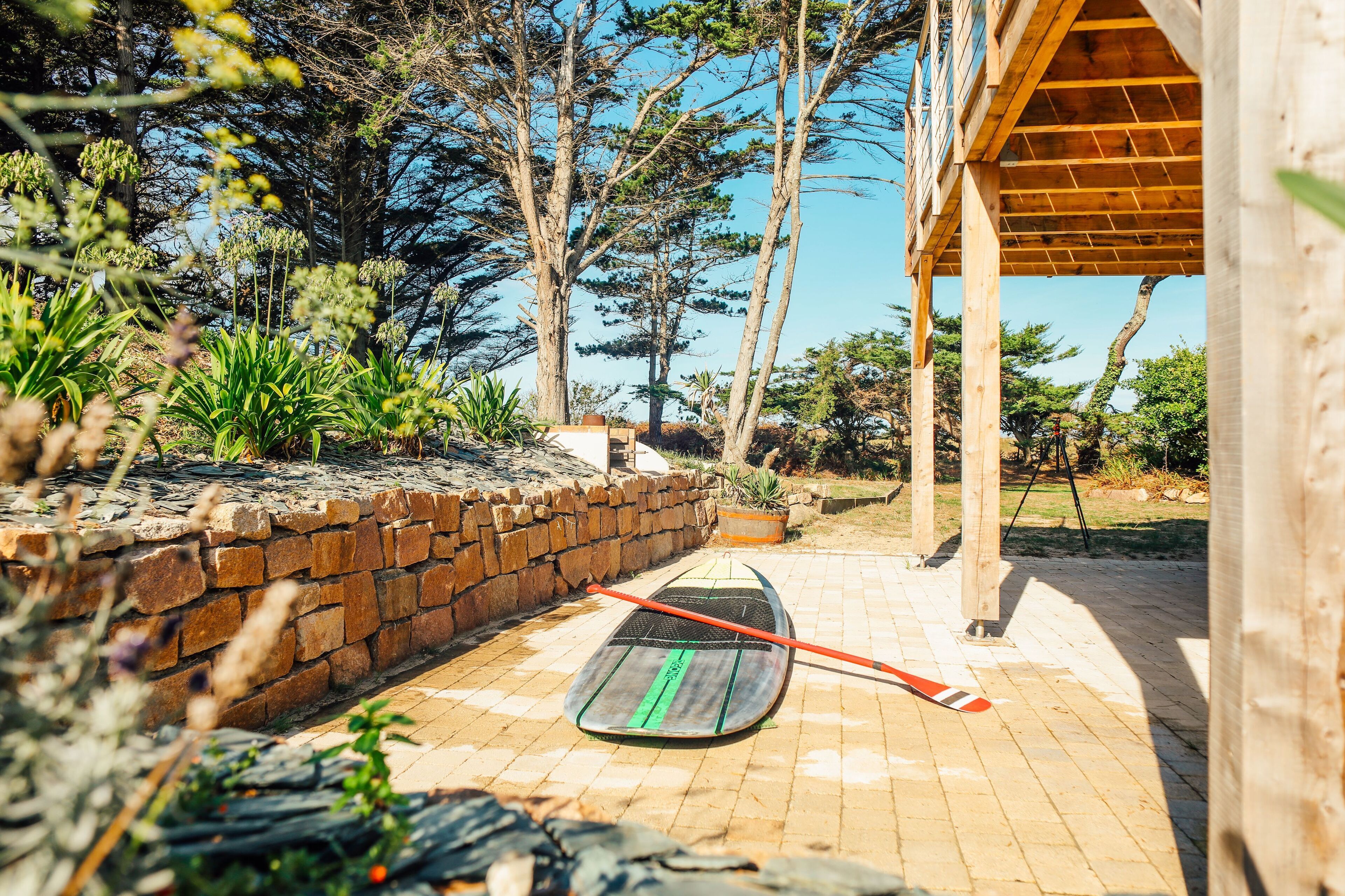 Une planche de paddle sur un patio en briques, avec un mur en pierre et une pergola en bois.