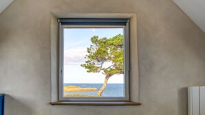 Et soveværelse med et vindue der kigger ud på et træ og havet.