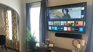 A living room with a flat-screen TV mounted on the wall displaying a video call interface. - Lower Greenville Studio (Dallas)