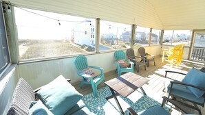 A covered outdoor seating area with chairs and tables, large windows with a view of buildings and a beach. - Perfect for Couples and Families - Amazing Ocean View Beach House (North Topsail Beach)