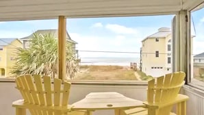 A room with two yellow Adirondack chairs and a small table, overlooking a beach and buildings. - Perfect for Couples and Families - Amazing Ocean View Beach House (North Topsail Beach)
