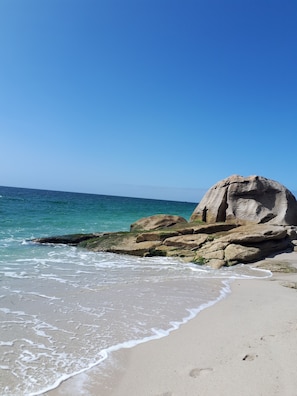 A beach with clear blue water, a large rock formation, and a sandy shore. - Renovated 2-star furnished apartment for 4 people   (Guilvinec)