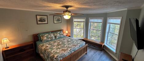 A bedroom with a wooden bed, a ceiling fan, and three windows.