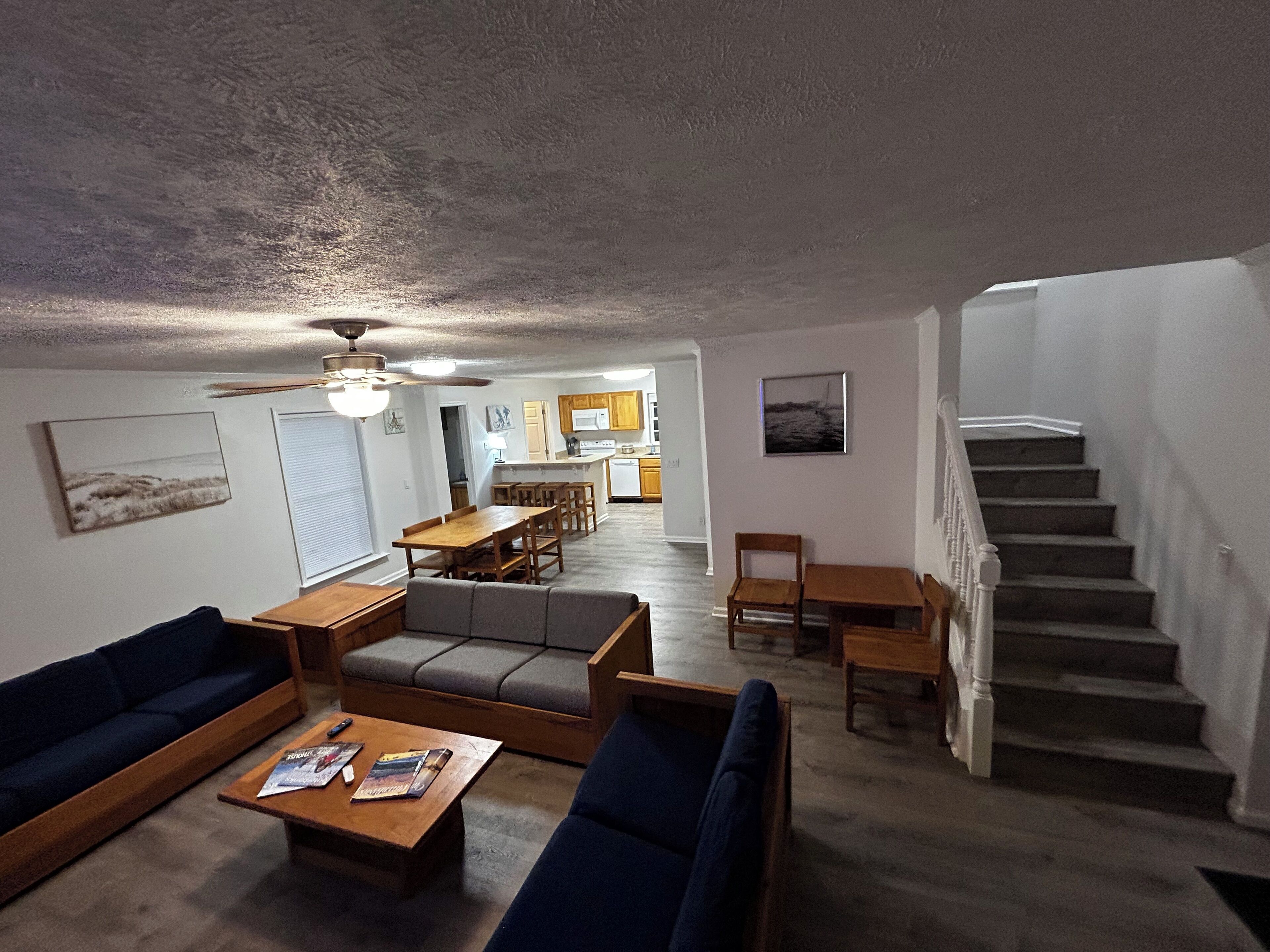 A living room with a sofa, coffee table, and a dining area with chairs and a table. There is a staircase leading to another level.
