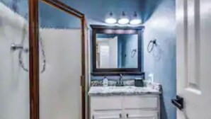 Un baño con ducha, lavamanos y espejo.