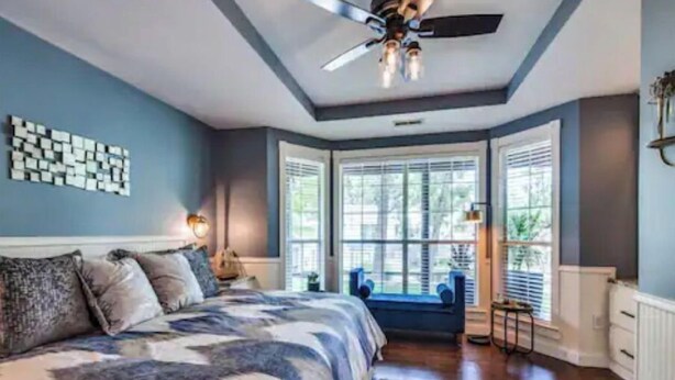 Un dormitorio con cama, ventilador de techo y ventana grande con persianas.