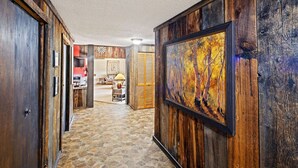 Un couloir aux murs en bois et au sol en pierre mène à un espace de vie doté d’une cheminée.