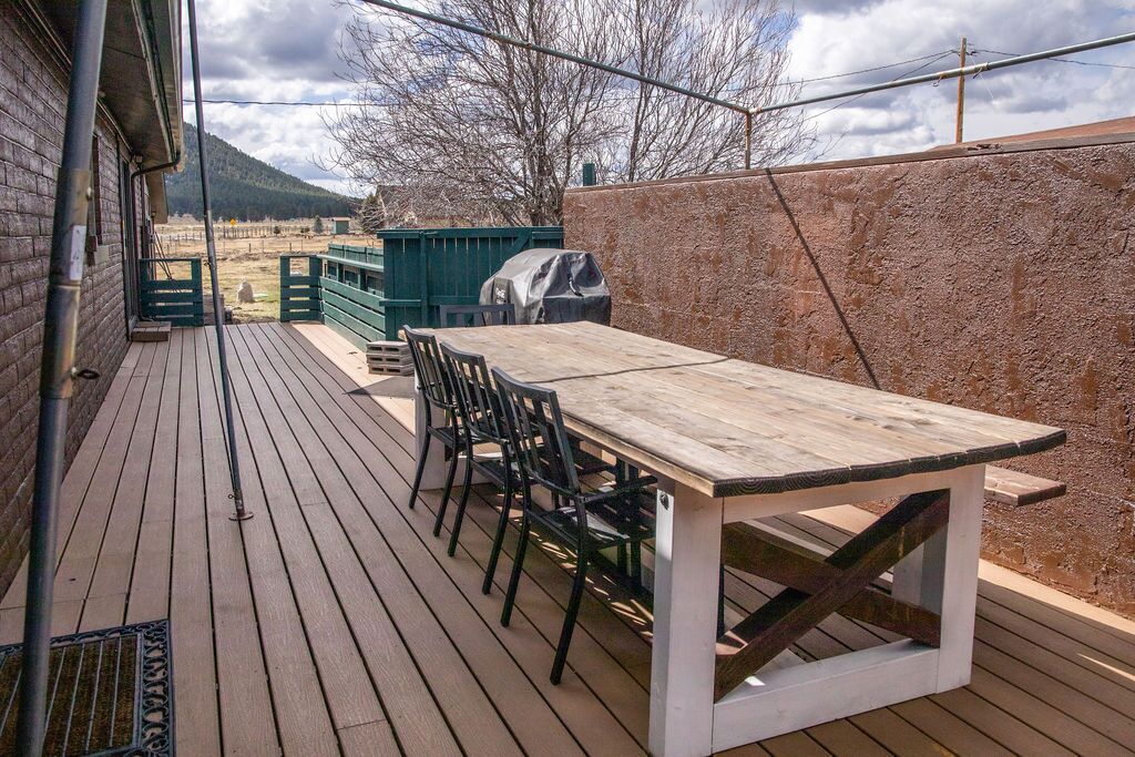 Eine Terrasse im Freien mit einem Holztisch und -stühlen, einem Grill und Blick auf eine Berglandschaft.