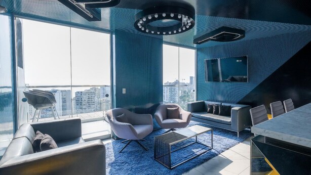 Un salon moderne doté d’une grande fenêtre, d’un canapé, de deux fauteuils, d’une table basse et d’une table à manger.