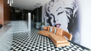 Un hall d’entrée moderne avec un sol à motifs noir et blanc, une grande fresque murale et un canapé incurvé agrémenté de coussins.
