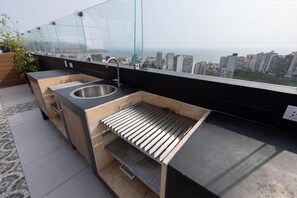 Una cucina sul tetto con lavello in acciaio inossidabile, barbecue integrato e veranda vetrata con vista sulla città.