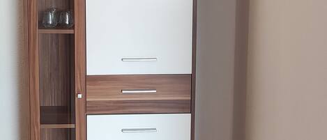 Ein Zimmer mit einem Holzschrank mit mehreren Einlegeböden und Schubladen, einer weißen Kommode und einem motivierenden Zitat an der Wand.