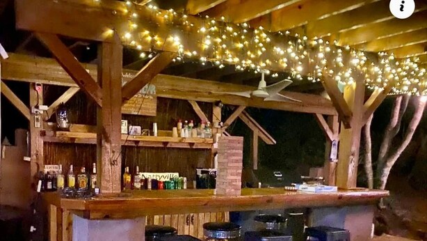 An outdoor bar area with a wooden structure, string lights, and several stools. - Surfer Shack 2 King Bedrooms (1 is a Loft) (East End)