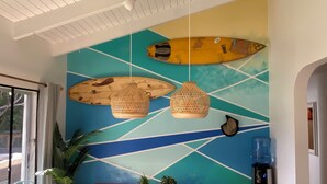 A dining area with a wooden table, hanging wicker lamps, and a colorful wall mural. - Surfer Shack 2 King Bedrooms (1 is a Loft) (East End)