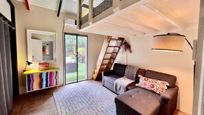 A spacious living area with a sofa, a colorful cabinet, a mirror, and a sliding glass door leading to a garden. - Surfer Shack 2 King Bedrooms (1 is a Loft) (East End)