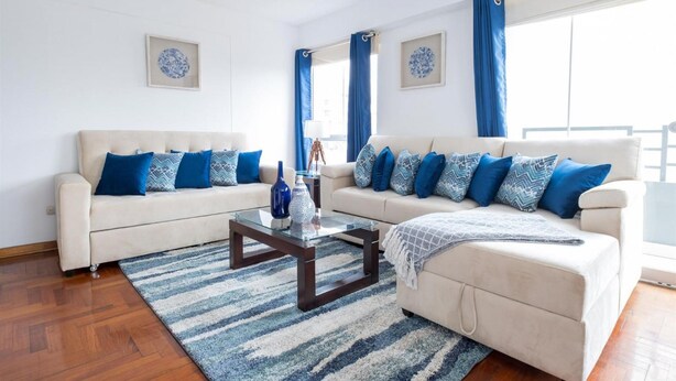 Una sala de estar con un sofá beige, una mesa de centro de vidrio y un tapete azul y blanco a rayas.