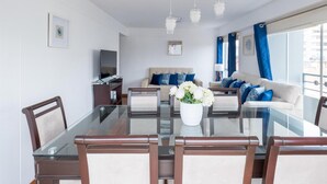 Una sala moderna con una mesa de comedor de vidrio, sofá color beige y cortinas azules.