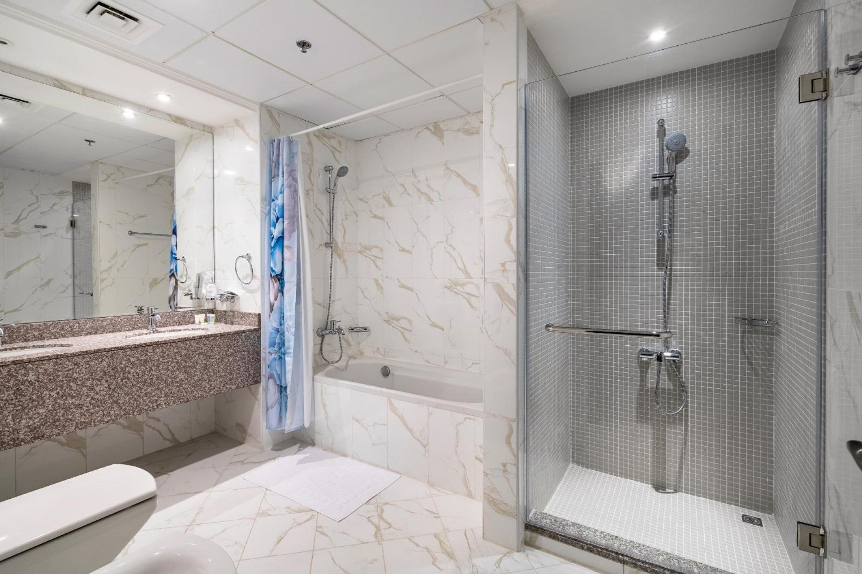 A modern bathroom with a marble vanity, a bathtub, a shower enclosure, and a large mirror.