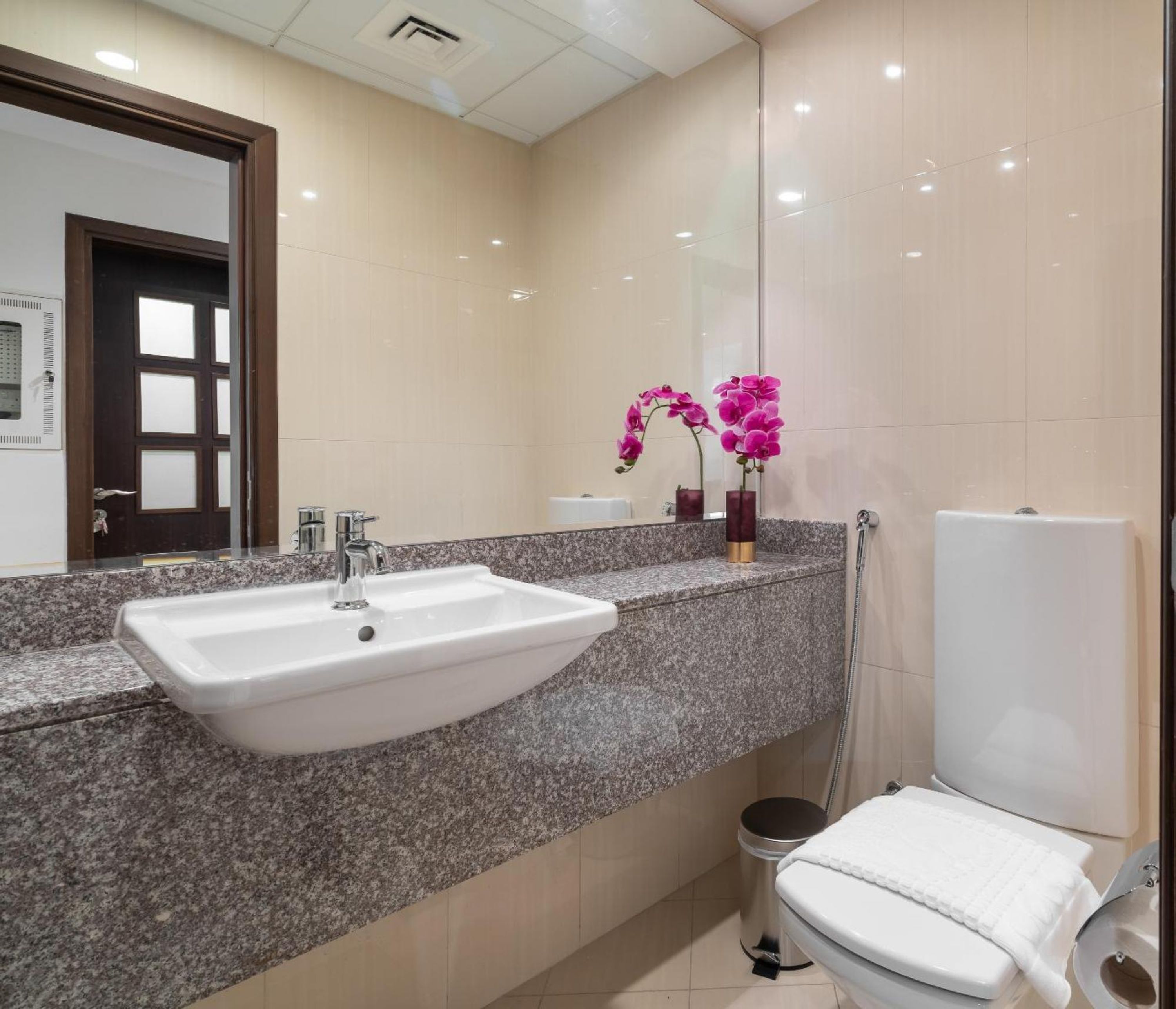 A modern bathroom with a granite countertop, a white sink, a glass shower enclosure, and a white toilet.