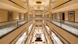 Un hall d’hôtel à plusieurs niveaux, doté d’un atrium central, de rampes en verre et d’un lustre.