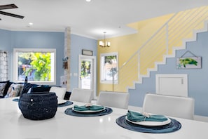 Uma área de refeições com uma mesa branca posta para dois, uma cesta trançada azul e uma escada com degraus amarelos.