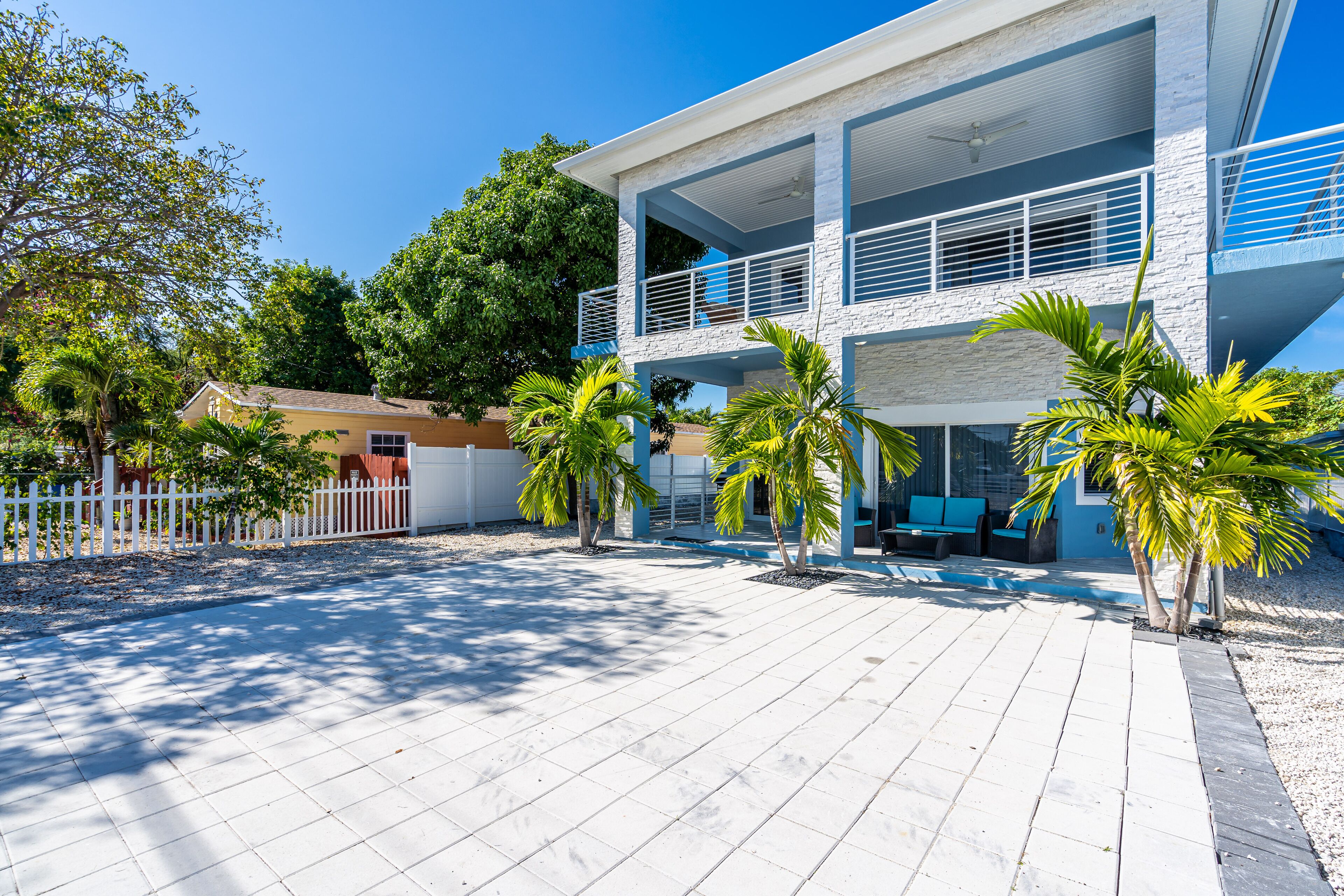 A modern two-story house with a balcony, a pool area, and a white picket fence.