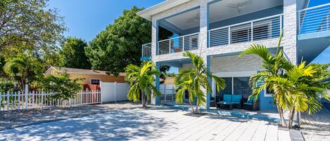 A modern two-story house with a balcony, a pool area, and a white picket fence.
