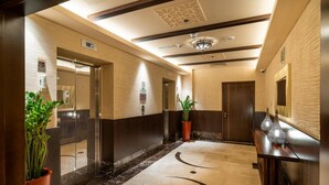 Una hall d'albergo moderna con pavimento in marmo, pannelli in legno e reception con vasi decorativi.