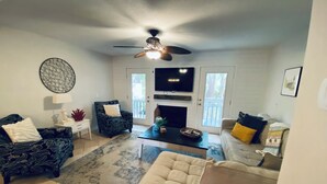 Una sala de estar con ventilador de techo, chimenea, televisor y puerta que da al exterior.