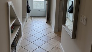 Un pasillo con piso de baldosas, una puerta que da al exterior y un espejo en la pared.
