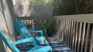 Un patio cubierto con dos sillas Adirondack turquesa, un tapete estampado y una valla de madera.