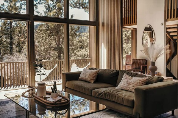 A modern living room with a sofa, a glass coffee table, and a view of a balcony with a wooden railing.