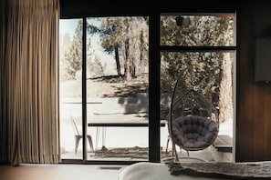 A room with a large window, a hanging chair, and a bed.