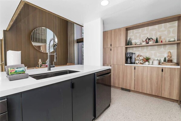 A modern kitchen with a central island, wooden cabinets, a built-in oven, and a round mirror above the sink.