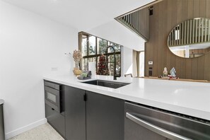 Une cuisine moderne dotée d’un grand îlot central, d’un four encastré et d’une fenêtre donnant sur la verdure.