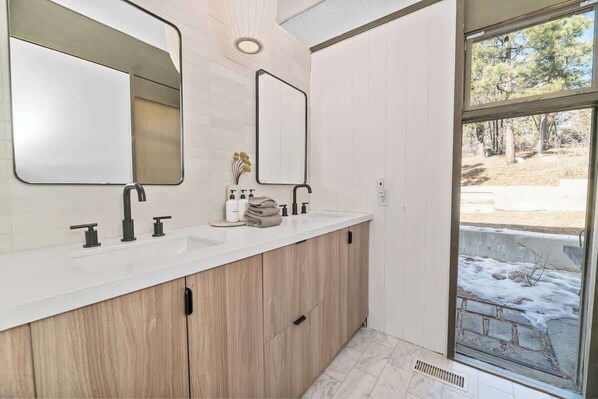 Un baño con dos lavamanos, armarios de madera, un espejo y vistas a un paisaje invernal nevado.