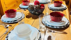 A wooden dining table set with plates, bowls, and cutlery, with a 'Welcome' sign and a Coca-Cola sign in the background.