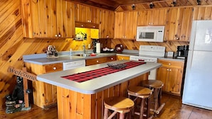 A kitchen with wooden cabinets, a central island with stools, a microwave, and a refrigerator.