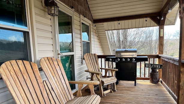 A wooden deck with Adirondack chairs, a barbecue grill, and a welcome sign.