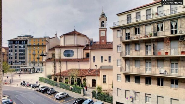 Un edificio de varios pisos con una torre de reloj, coches aparcados y vista de la calle.
