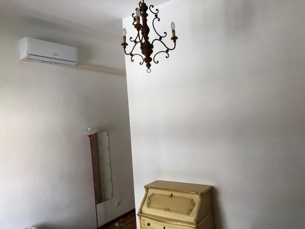 Una habitación con un equipo de aire acondicionado blanco, una lámpara de araña oscura y ornamentada, un espejo y un pequeño aparador beige.